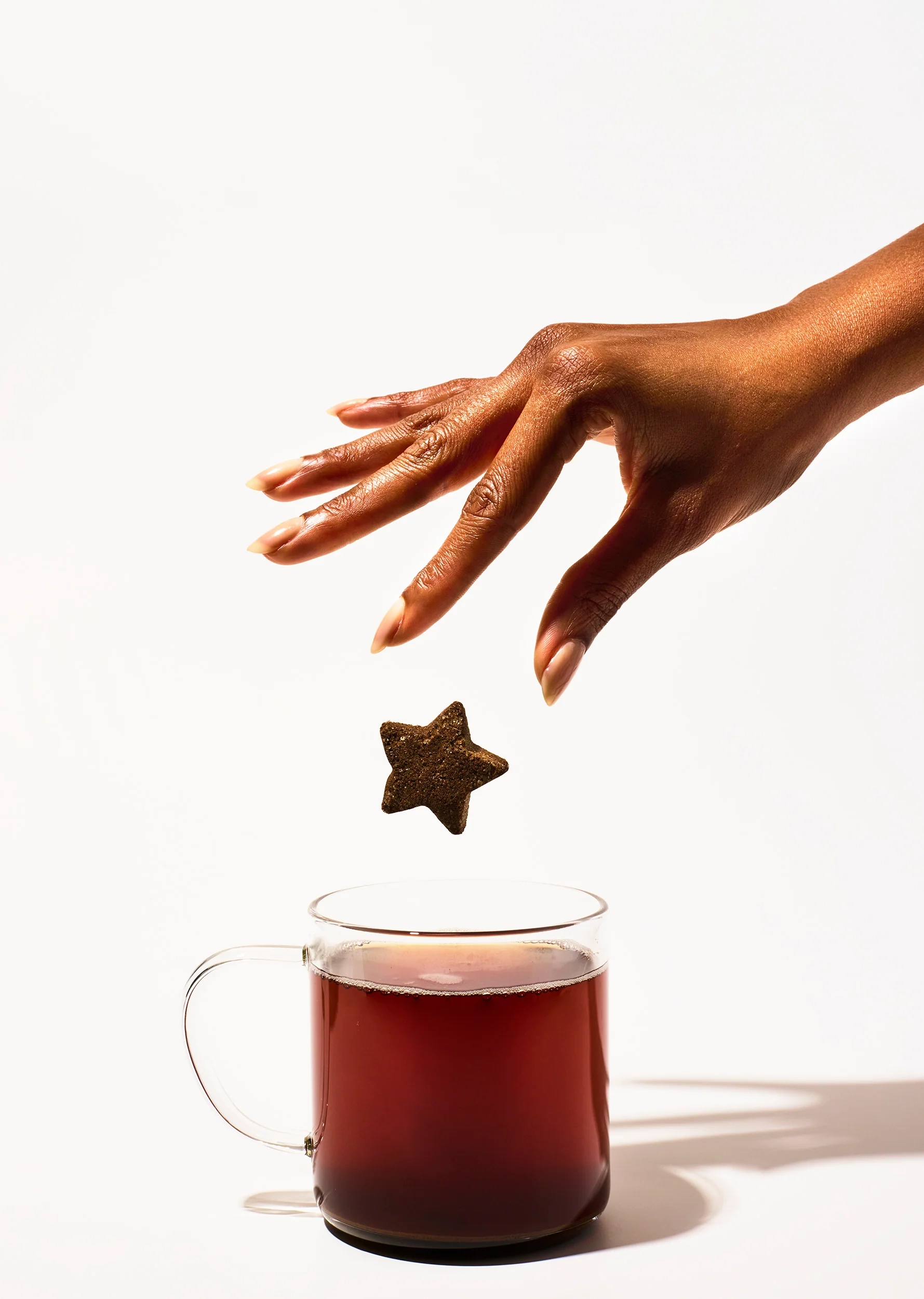 A hand drops a star-shaped Tea Drop into a glass mug of hot tea
