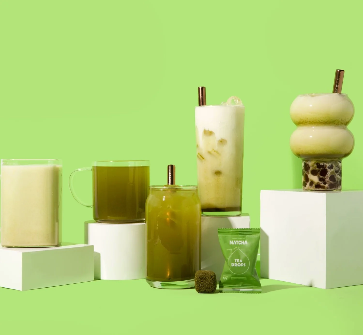 Matcha and milk tea drinks on green pedestals with Tea Drops