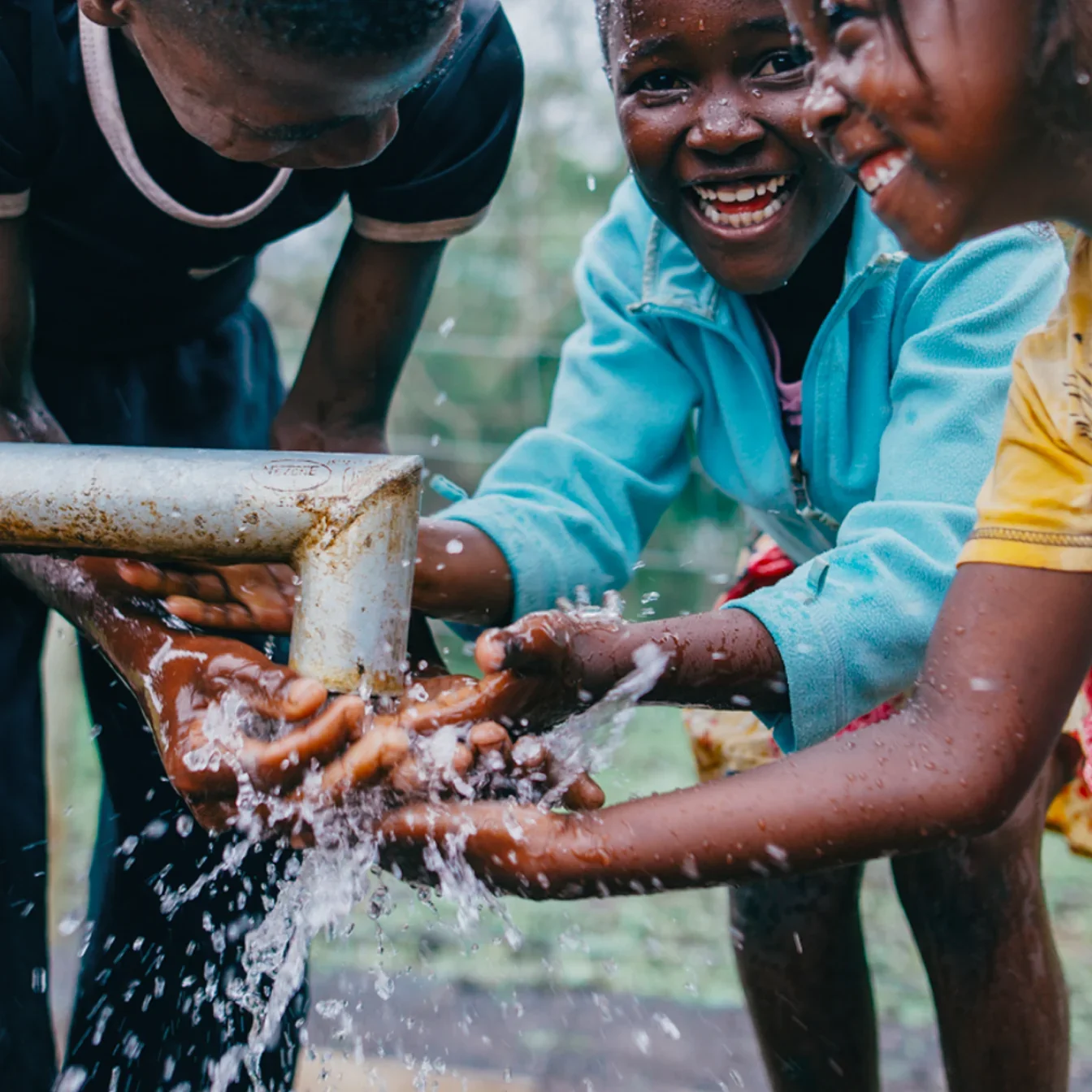 Children smiling at a water tap